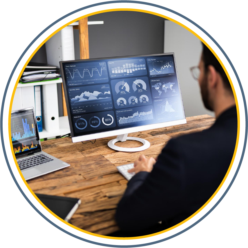 A person sat at a wooden desk working on an computer with graphs on it.